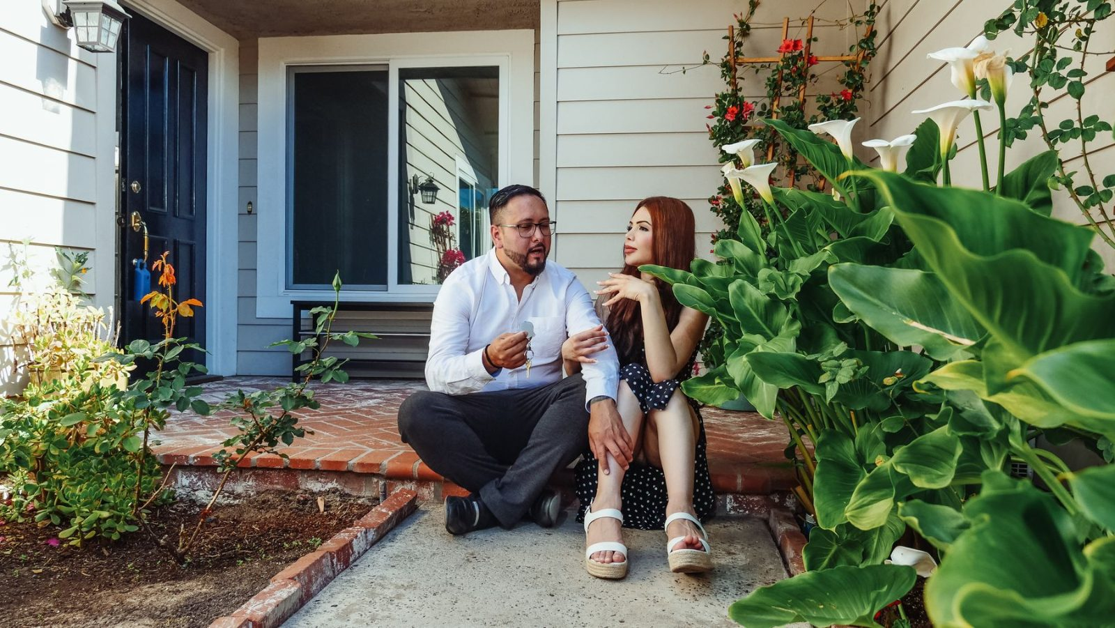 Couple sitting together on the front steps of their home surrounded by tropical plants