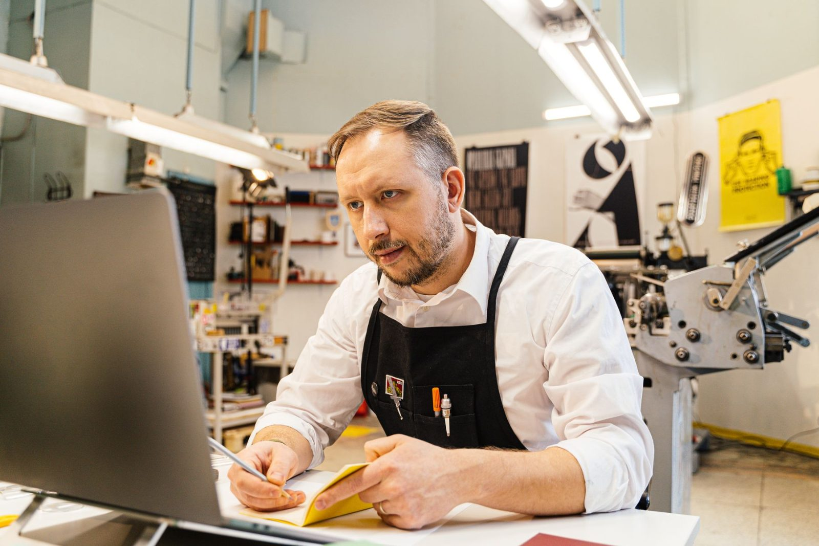 Self-employed print shop owner reviewing paperwork at his laptop in his workshop