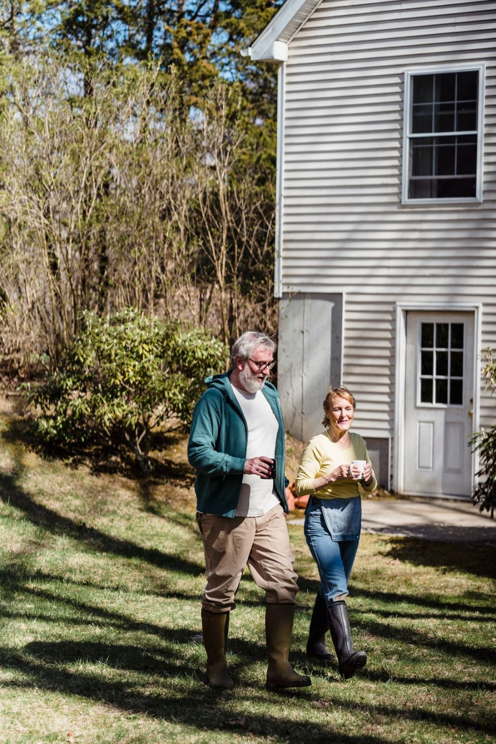 Active older couple walking together with coffee mugs outside their home on a sunny morning